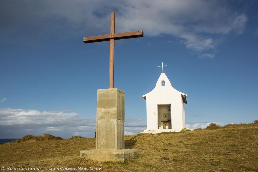 Imagem do crucifixo e ao fundo a Capela de São Pedro em Fernando de Noronha.